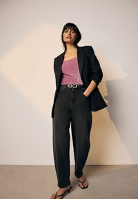 Zwarte blazer over een roze top met structuur, gecombineerd met zwart high-waist spijkerbroek en zwarte slippers; gladde stoffen en een ontspannen pasvorm.