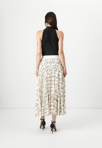 Haut halter plissé noir avec une jupe blanche ornée d'écriture noire en cursive, assorti à des chaussures à talons carrés noires, vu de dos.