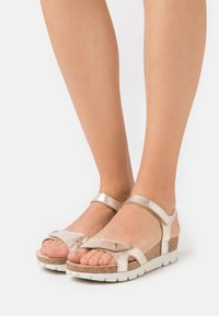 Σανδάλια σε σχήμα σφήνας με μεταλλικές χρυσές λωρίδες, υφασμάτινη μεσαία σόλα από φελλό, άσπρη ελαστική σόλα και σχεδίαση στρογγυλής μύτης με κομμένες λεπτομέρειες.