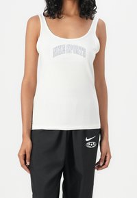 Bílý top na ramínka s nápisem "NIKE SPORTS" napsaným šedě, úzké ramínka a hladká, lehká látka. V kombinaci s černými kalhotami.