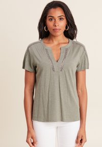 Olijfgroen shirt met korte mouwen heeft een diepe V-halslijn met kantdetails langs de hals en schouders. Zacht, soepel vallend materiaal.
