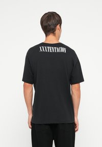 Czarny bawełniany t-shirt z krótkim rękawem i okrągłym dekoltem, z napisem "XXXTENTACION" nadrukowanym dużymi białymi literami na plecach.