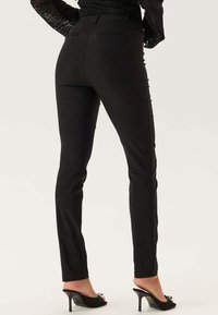 Pantalons noirs slim en tissu doux, avec une texture lisse, des poches arrière et un design épuré et tailleur.
