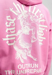 Sudadera rosa con gráficos blancos que presentan un caballo y un guerrero, el texto dice "persigue la primera luz" y "sobrepasa a los desprevenidos."