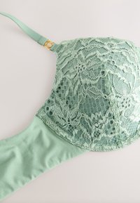 Nėrinių liemenėlė švelnios žalios mėtų spalvos su gėlių raštais, lygiu audiniu, reguliuojamomis petnešėlėmis ir auksinės spalvos detalėmis.