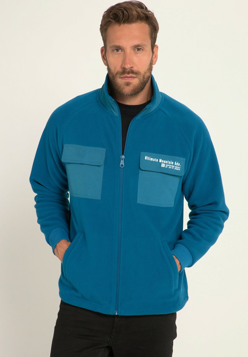 Giacca in felpa turchese con colletto alto, zip frontale, due tasche sul petto e tasche laterali. Presenta dettagli in tessuto a contrasto sulle tasche.