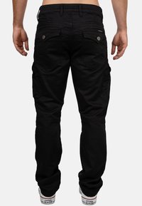 Pantaloni cargo neri con multiple tasche, dettagli in bottone e un tessuto testurizzato, caratterizzati da una vestibilità affusolata e orli cuffati.