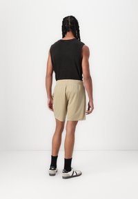 Beige mesh shorts med elastisk talje, parret med en sort ærmeløs skjorte og sorte knæsokker, set fra ryggen.