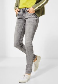 Upnuté šedé džíny z denimu s mírně vybledlým vzhledem, pěti kapsami a zapínáním na knoflík. V kombinaci s bílými teniskami.