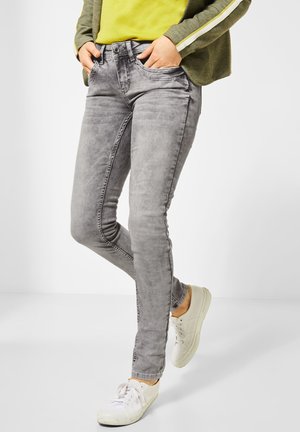 Strakke grijze spijkerbroek van denim, met een lichte vervaging, vijf zakken en een knoopsluiting. Gecombineerd met witte sneakers.