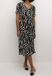 Robe noire et blanche avec un motif à rayures zébrées, manches courtes, col en V profond, taille ceinturée et boutons sur le devant, réalisée dans un tissu fluide.