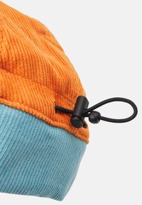 Corduroy hat with an orange top and a blue bottom. Features a textured surface and a black drawstring toggle for adjustment.