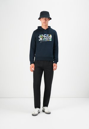 Marineblaues Hoodie mit "JACK & JONES"-Logo und bunten Akzenten, kombiniert mit schwarzen Hosen und weißen Sneakers mit schwarzen Streifen. Schwarzer Bucket Hat.