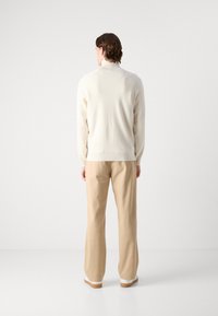 Crämd knitsweater med hög hals, i par med beige vida byxor. Enkelt mönster med en slät textur och minimal detaljer.