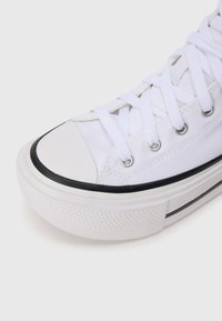 Sneaker bianco in tela con suola in gomma, punta nera e striscia nera sulla suola. Presenta lacci bianchi e occhielli in metallo.