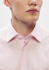 Ροζ ανοιχτόχρωμο πουκάμισο με κλασικό γιακά, που διαθέτει λεία υφή και δι�ακριτική γυαλάδα. Δύο κουμπιά ορατά στο μπροστινό μέρος.