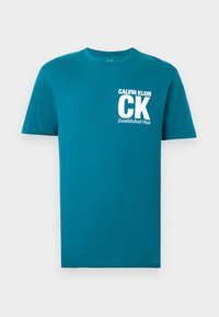 Tyrkysové bavlnené tričko s krátkymi rukávmi a okrúhlym výstrihom. Na ľavej strane na hrudi je biely nápis: "CALVIN KLEIN," "CK" a "Established 1968".