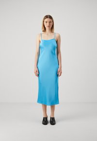 Sinine satiinist liibuva kleit õhukeste rihmadega, sirge lõikega ja sileda tekstuuriga, koos mustade puusadega kingadega. Minimalistlik ja elegantne välimus.