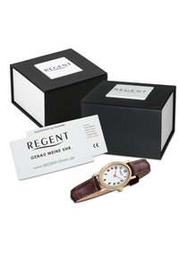 Montre dorée avec un cadran blanc, des chiffres arabes noirs et un bracelet en cuir marron, accompagnée d'un emballage noir et blanc et d'une carte de garantie.