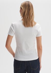Maglietta bianca a coste con maniche corte, forma aderente e scollo rotondo, abbinata a pantaloni in denim scuro, che mostrano una texture liscia.