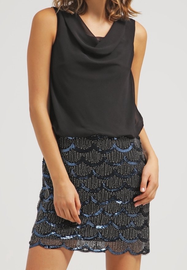 Femme portant un haut noir sans manches et une mini-jupe noire avec des motifs en sequins bleu et argent en forme de coquilles.