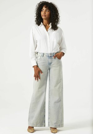 Witte blouse met lange mouwen, lichtblauwe broek met wijde pijpen en gouden ballet flats. Soepele stoffen met een relaxte pasvorm en een detail van een voorzak.