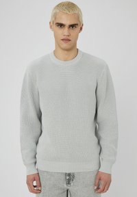 Pull en maille gris clair texturé avec un col rond, des poignets côtelés et un ourlet côtelé. Tissu tricoté, coupe décontractée et manches longues.