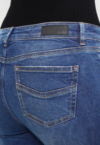Vaqueros de mezclilla azul con una cintura alta, que cuentan con costuras en contraste y una etiqueta de cuero negra en la parte posterior. Dos bolsillos traseros visibles.