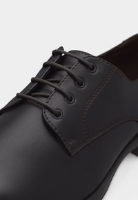 Μαύρο δερμάτινο επίσημο παπούτσι με κλειστό κορδόνι, στρογγυλή μύτη και ορατή ραφή στα τμήματα του τέταρτου και του άνω μέρους.