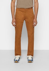 Brązowe bawełniane spodnie o prostym kroju z przednimi kieszeniami. Noszone z kolorowymi butami sportowymi z niebieskimi, białymi i żółtymi akcentami.