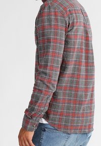Camicia in flanella a scacchi rossi e grigi con maniche lunghe, polsini con bottone e girovita curvo, realizzata in un tessuto morbido e testurizzato.