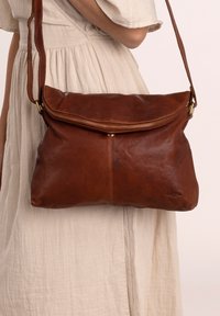 Brown leather shoulder bag with a zip closure and fold-over flap. It features a smooth texture and a gold-tone hardware accent.