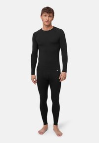 Schwarzes Thermo-Oberteil mit langen Ärmeln und Leggings, enganliegendes Design, glatte Textur, minimale Markenkennzeichnung am unteren Saum, geeignet zum Schichten.
