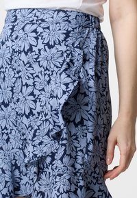 Gonna floreale in blu navy e blu chiaro, con dettagli arricciati e una vita elastica. Realizzata in tessuto leggero con una texture morbida.