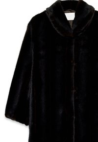 Čierny kabát z umelého kože s šálovým golierom, s mäkkou, lesklou textúrou a voľne strihanými rukávmi, zavesený na bielom vešiaku.