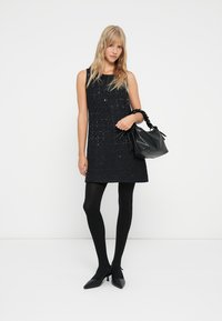 Robe noire sans manches avec un tissu texturé et des embellissements en sequins, associée à un sac à main noir et des collants opaques. Escarpins noirs pointus.
