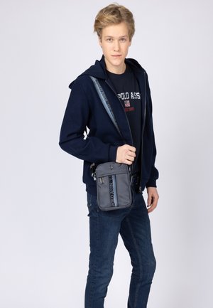 Borsa a tracolla grigia con una texture liscia, dotata di una tracolla con logo, compartimenti con zip e un sottile dettaglio del logo.
