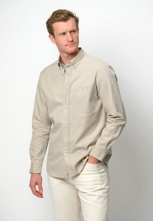 Beige langærmet skjorte med knapper og en brystlomme, lavet af et glat stof. Kombineret med lyse bukser med en afslappet pasform.