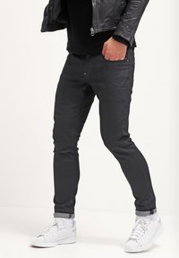Zwarte slim-fit broeken van denim, met een gladde textuur, metalen knopen en omgeslagen zomen, gecombineerd met witte sneakers.