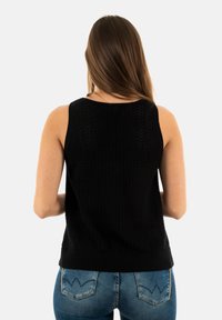 Top sans manches en tricot noir avec un motif en chevrons, encolure ronde et ourlet côtelé. Associé à un jean bleu, mettant en avant un design ajusté.