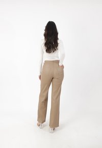 Beige wijde broek gemaakt van een glad materiaal, met achterzakken en een hoge taille, gecombineerd met een aansluitend wit langemouwen shirt.