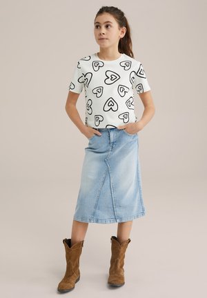 T-shirt blanc à manches courtes avec motif de cœurs noirs, associé à une jupe en denim bleu clair et des bottines en suède marron.