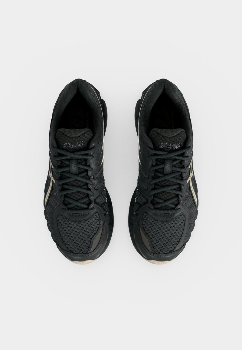 Par de zapatillas negras deportivas para correr con empeines de malla, cordones atados y detalles beige, vistas desde arriba sobre fondo blanco.