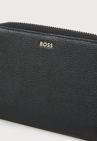 Zwarte leren portemonnee met een gestructureerd oppervlak, voorzien van een gouden "BOSS" logo en een ritssluiting. Eenvoudig ontwerp zonder zichtbare patronen.