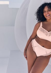 Lyserødt lingerisæt med blonder på bh'en og trusserne, med en glat stoftekstur og blomsterdekorationer langs kanterne.