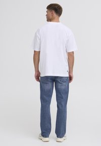 T-shirt en coton blanc à manches courtes, avec un col rond. Associé à un jean en denim bleu clair et des baskets beiges.
