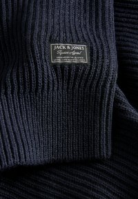 Tejido de punto acanalado azul oscuro con una etiqueta cosida en blanco y negro de "Jack & Jones Superior Apparel".