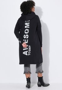Zwarte lange hoodie met de tekst "AWESOME TODAY" in vet, versleten witte letters op de achterkant. Gecombineerd met grijze cropped, gefranjerde jeans en zwart leren laarzen met studs.