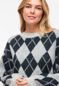 Pull à motif argyle gris et noir en fil texturé, avec un col rond et des manches longues, comprenant des poignets larges et une coupe décontractée.