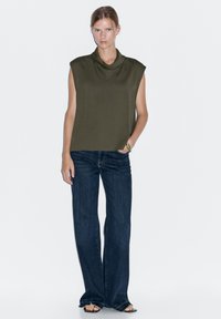 Oliwkowy bezrękawnik z drapowanym dekoltem, w połączeniu z ciemnoniebieskimi dzwonami. Prosty design, miękki materiał i luźny krój.